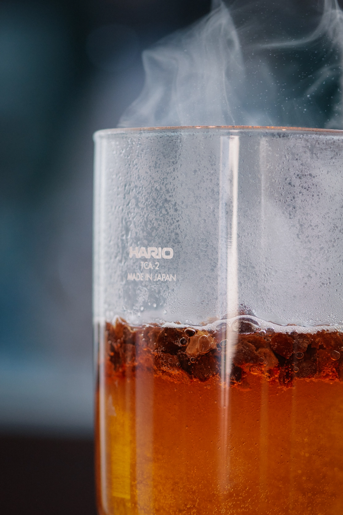 Steaming hot coffee brewing with ground beans in a glass Hario container.