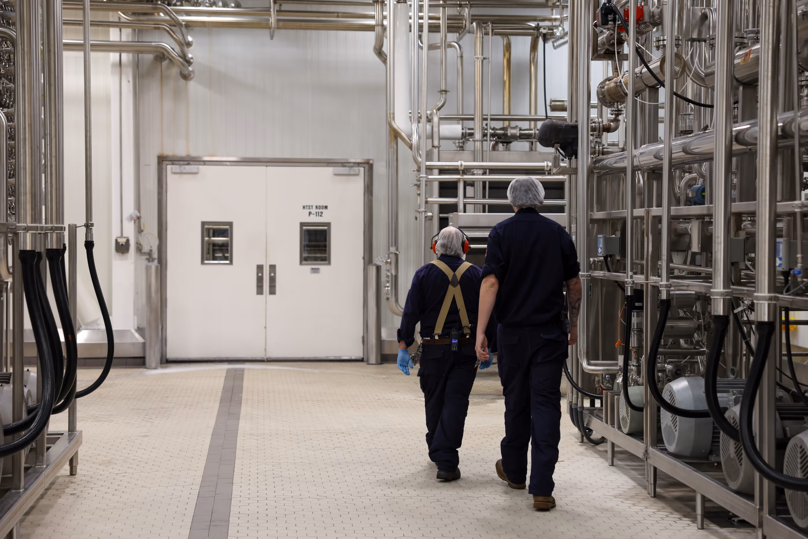 Two employees walking down an aisle at the plant with metal pipes on either side of them
