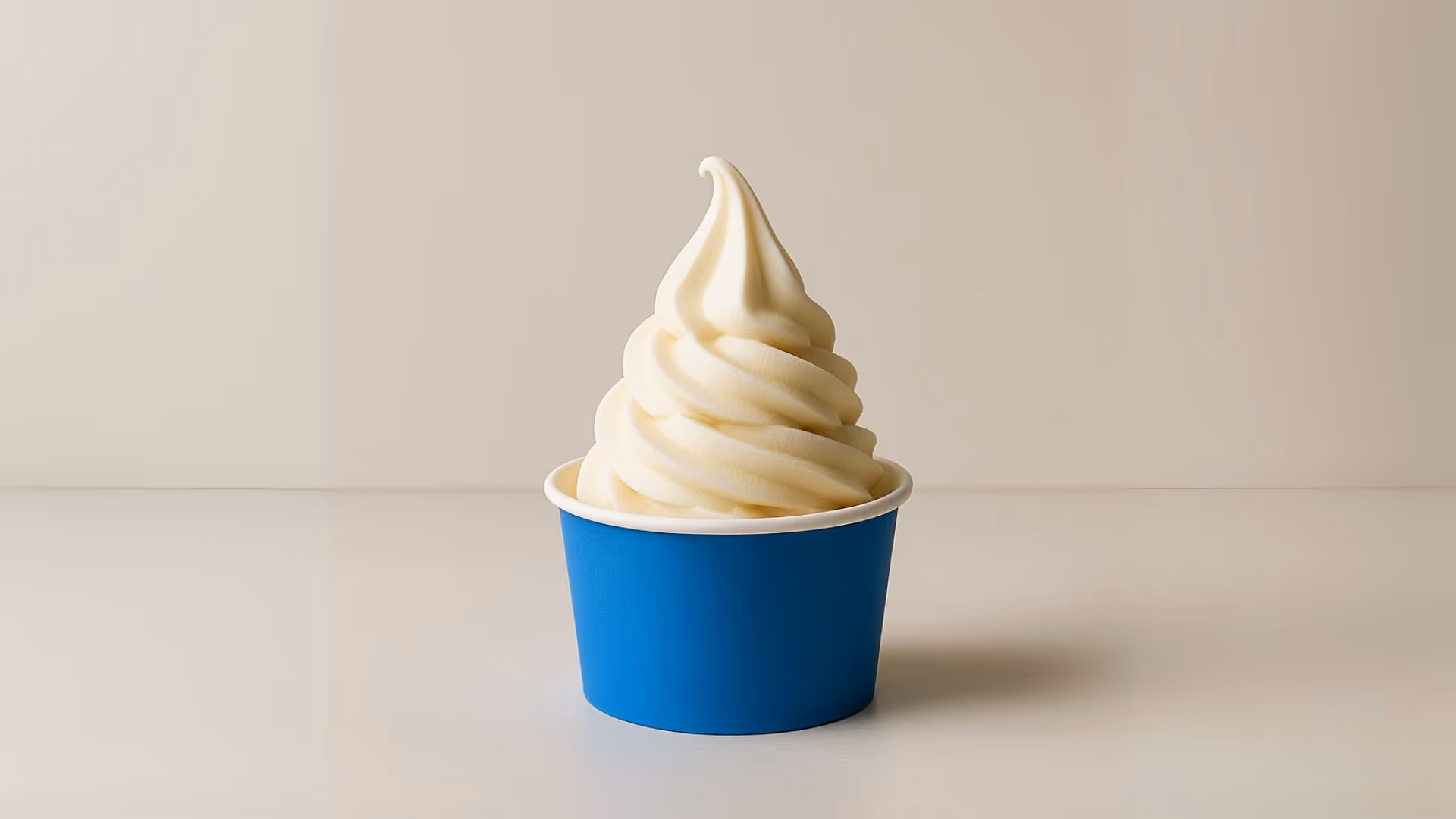 Swirled soft serve vanilla ice cream in a blue paper cup on a light surface and background.