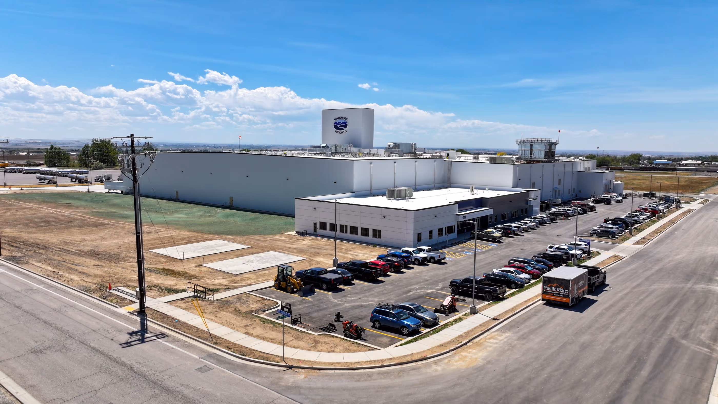 Idaho Milk Products plant with parking lot, various cars, trucks, and clear blue sky above.