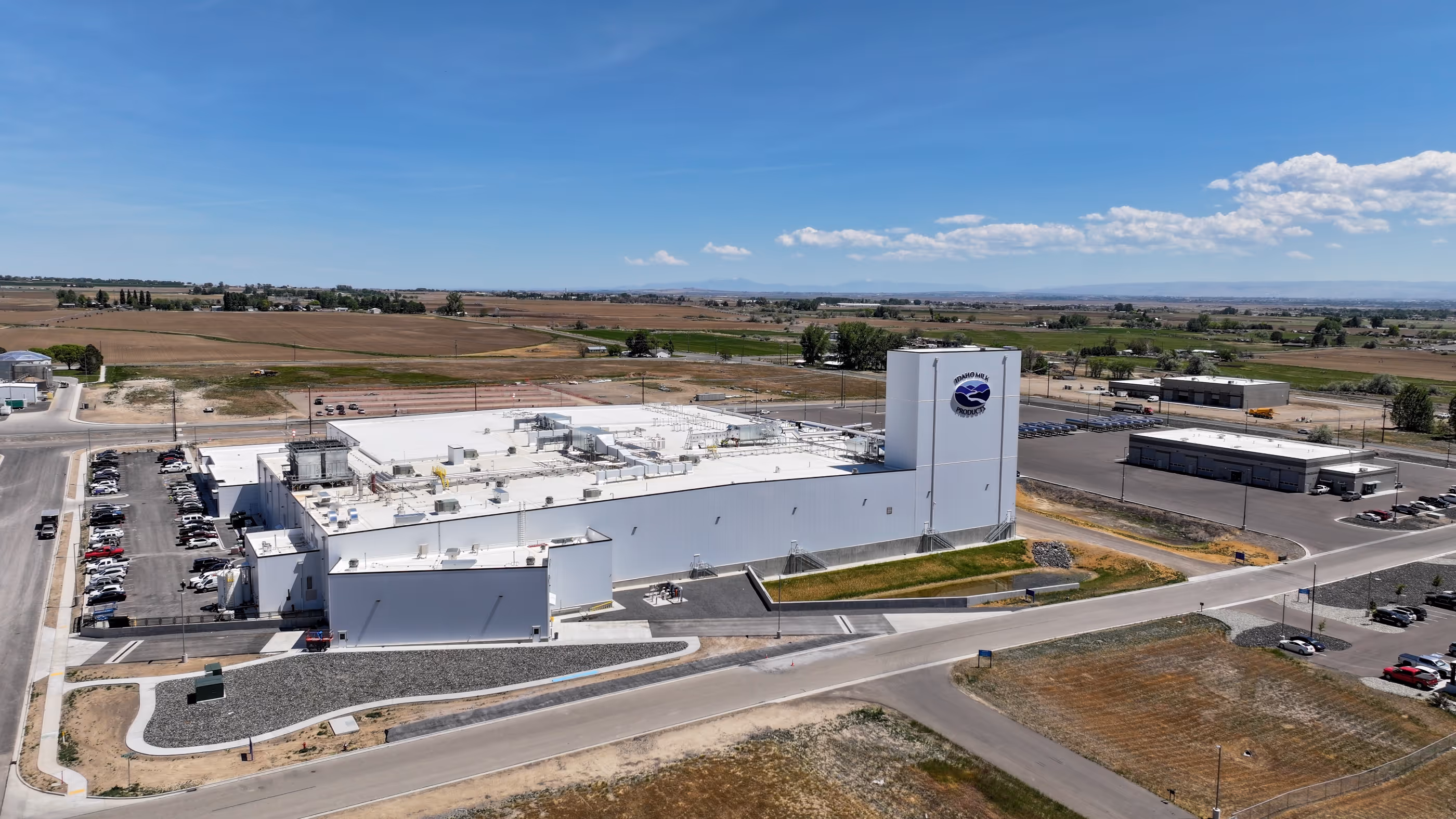 Large white industrial building with Idaho Milk Products logo surrounded by roads and farmland.