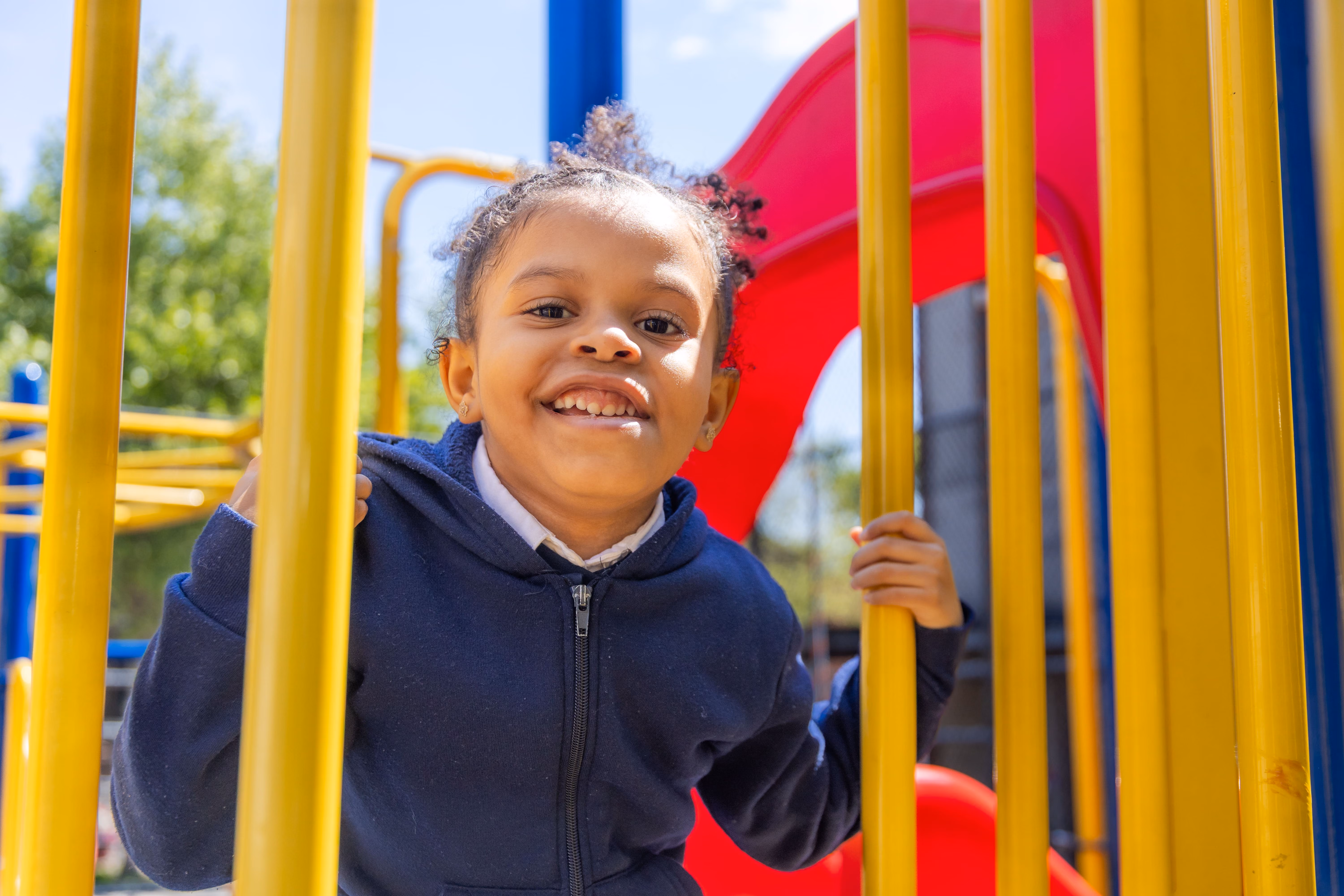 Smiling student in uniform playing on colorful school playground equipment
