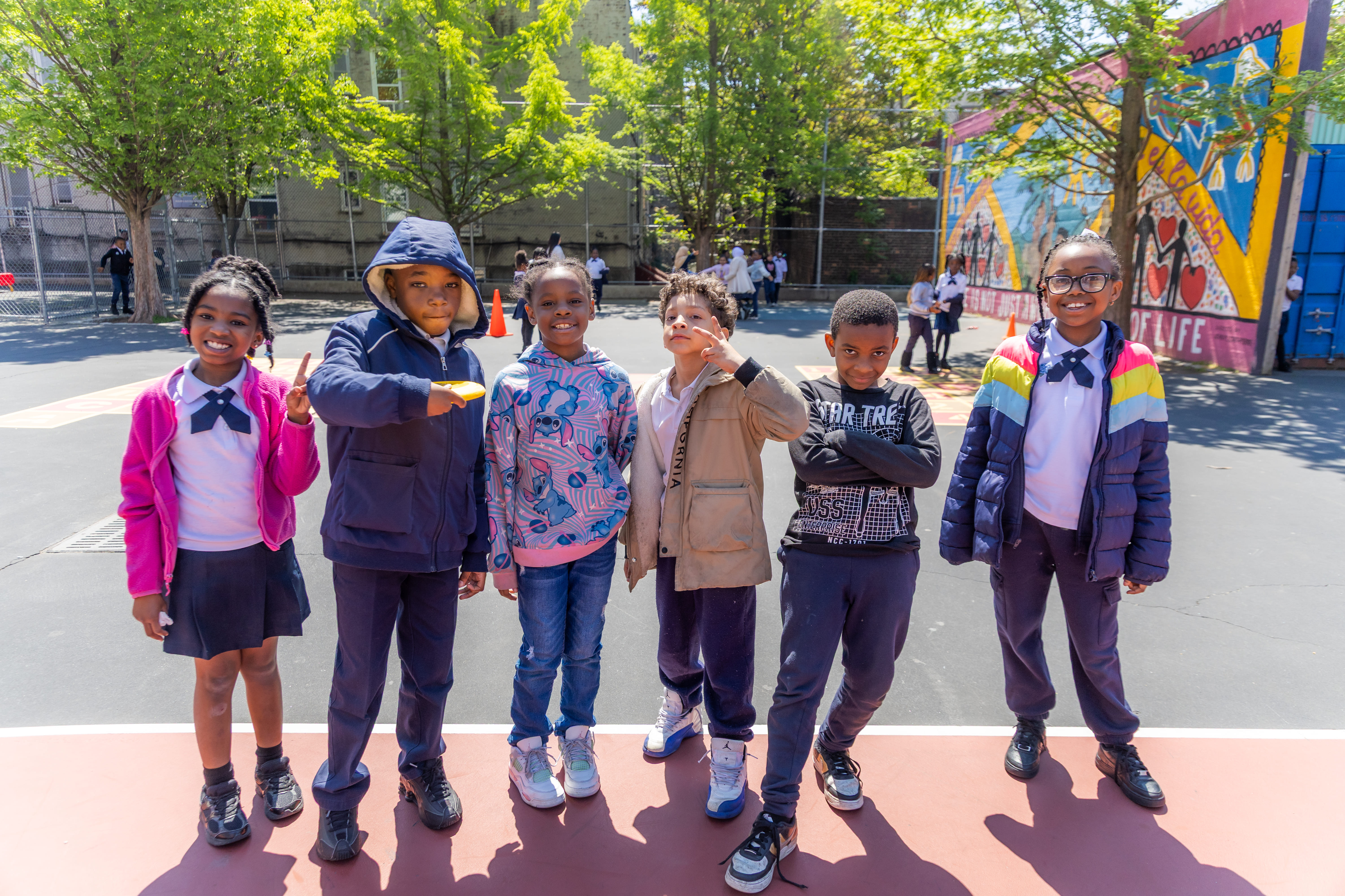 Six smiling students posing together on a sunny school playground
