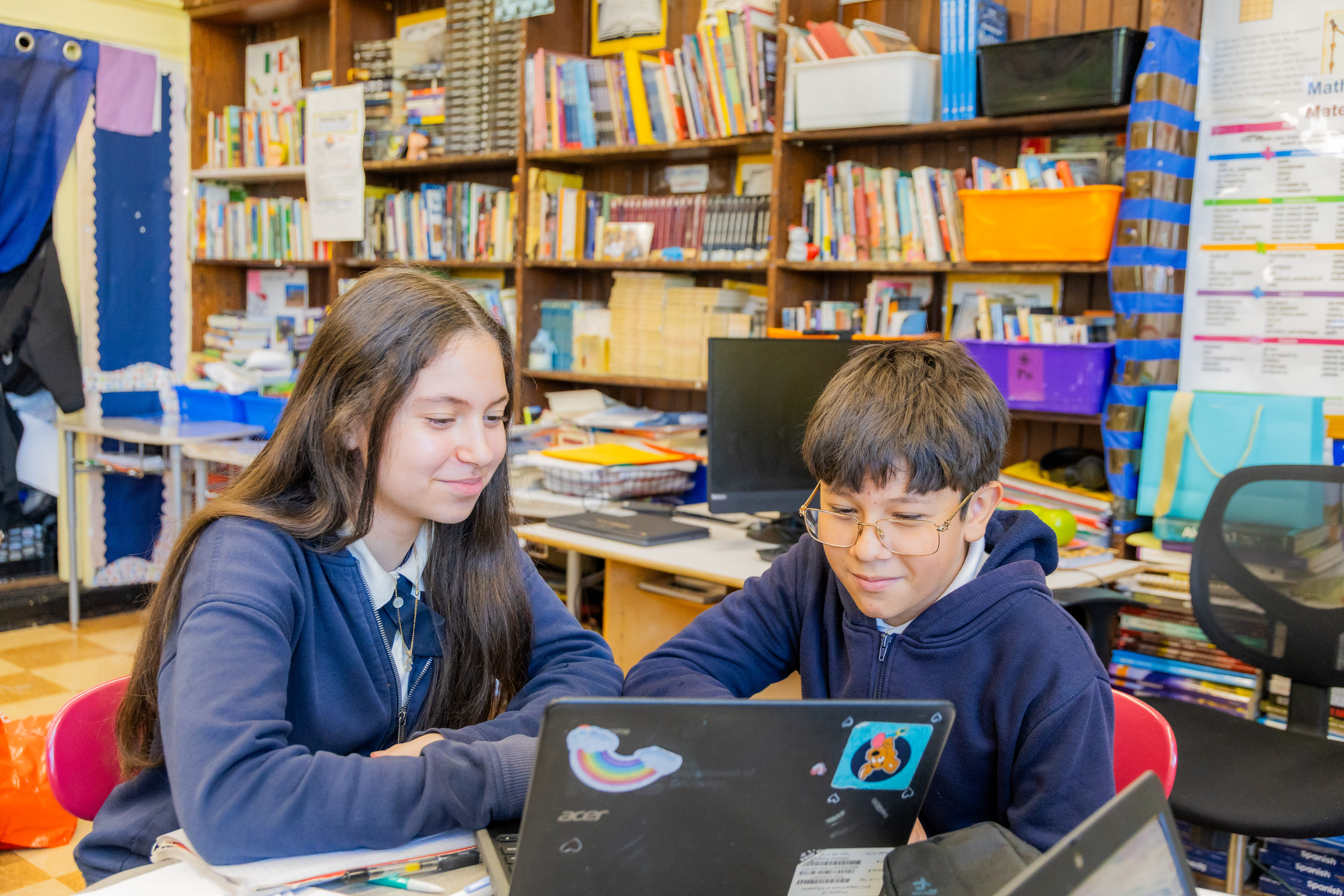 Two students collaborating on a laptop in a classroom library