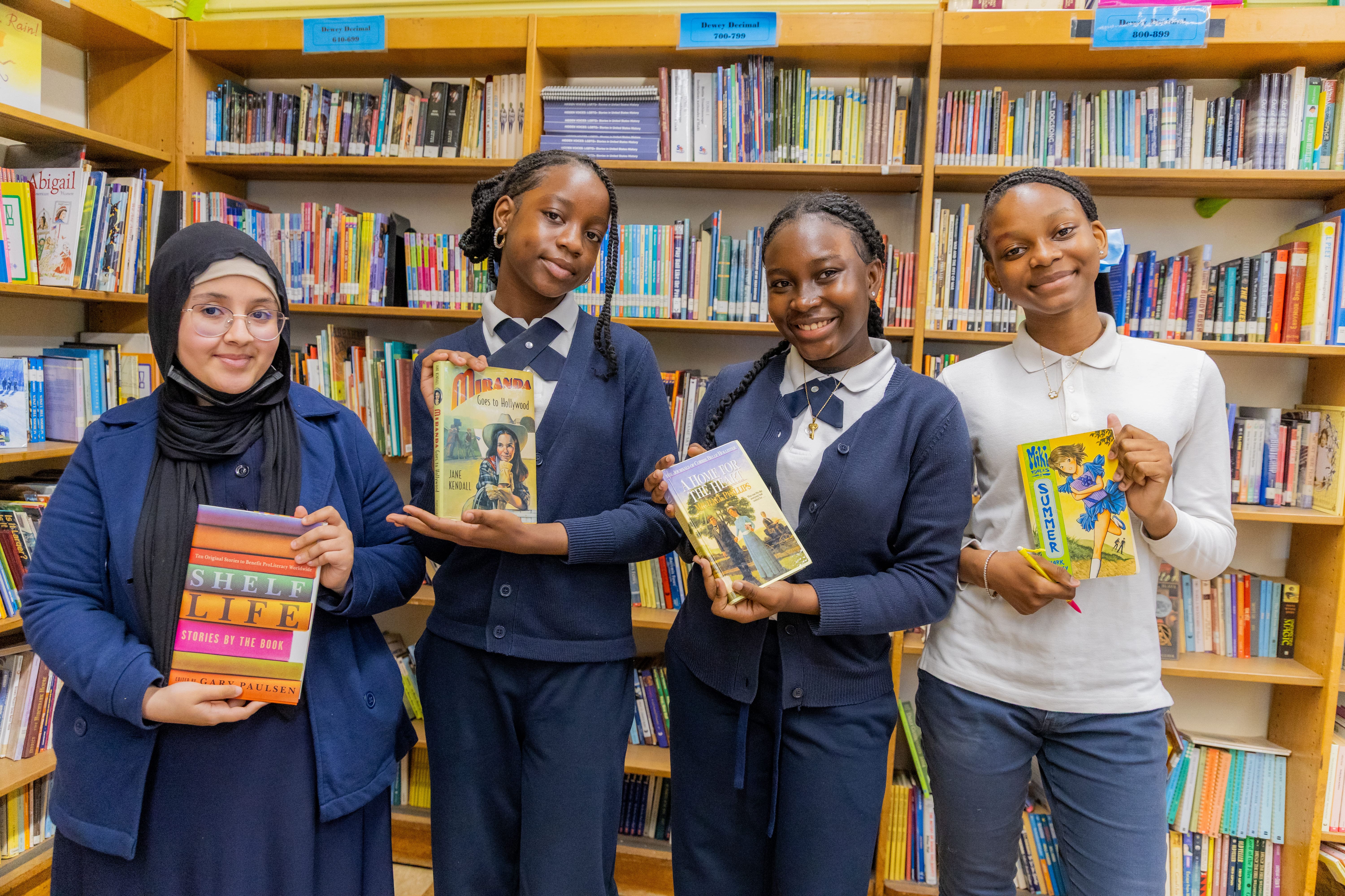 Four students holding books and smiling in school library