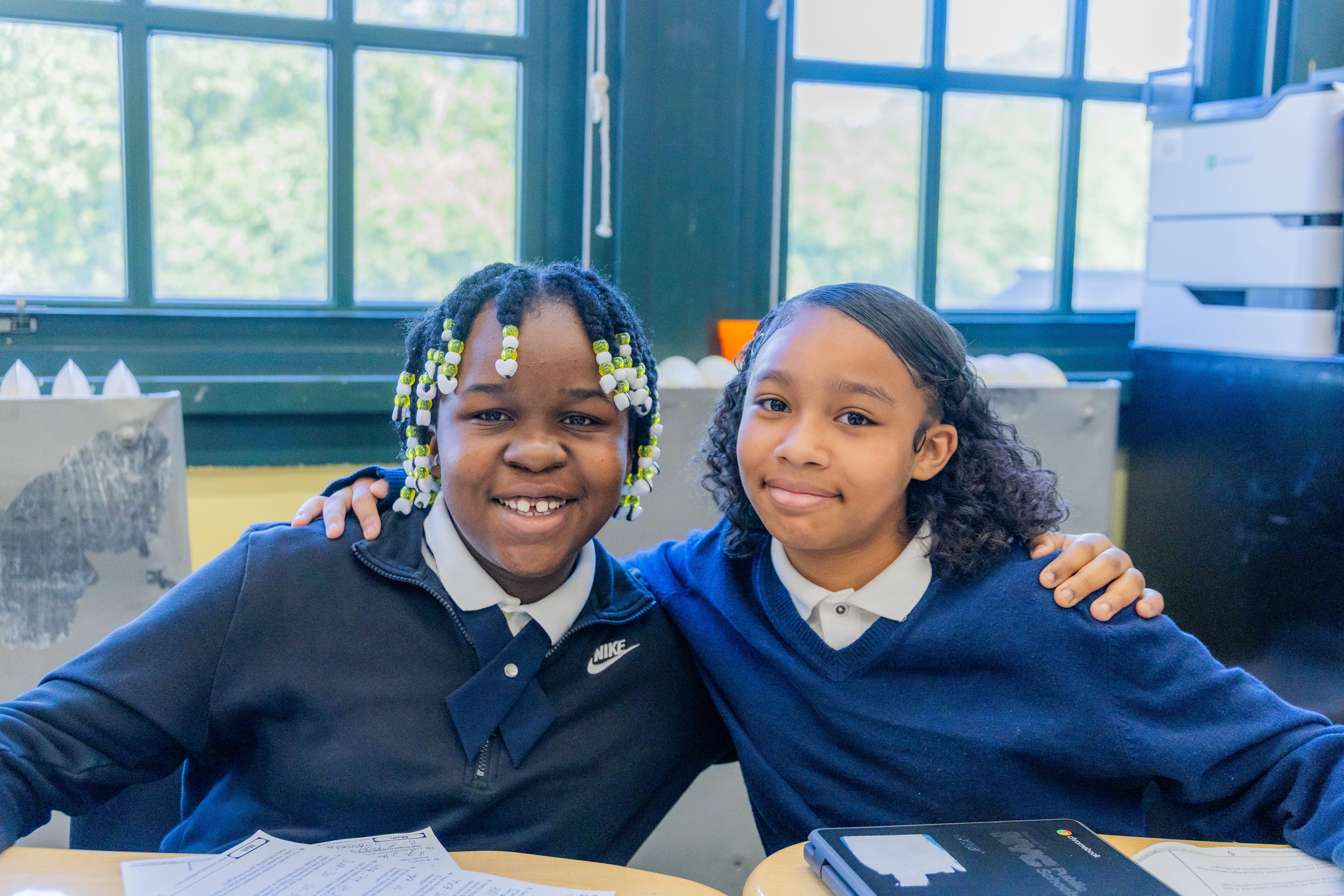 Two smiling students in school uniforms sitting together in classroom