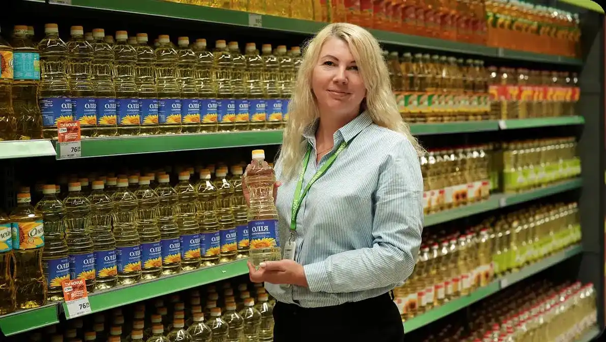 Працівниця NOVUS на тлі полиць з олією перевіряє якість продукції