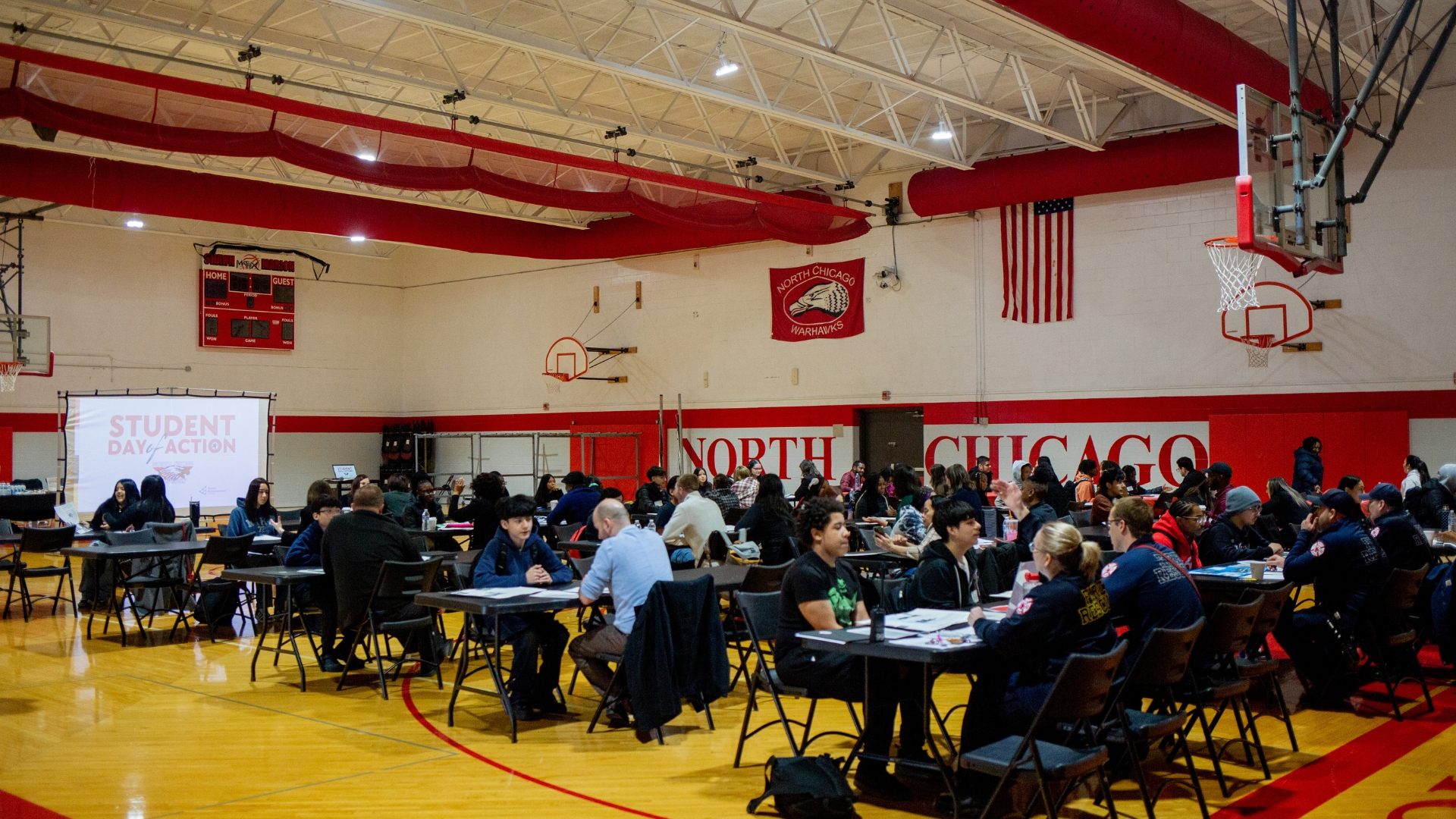 A group of people sitting at tables in a gym.