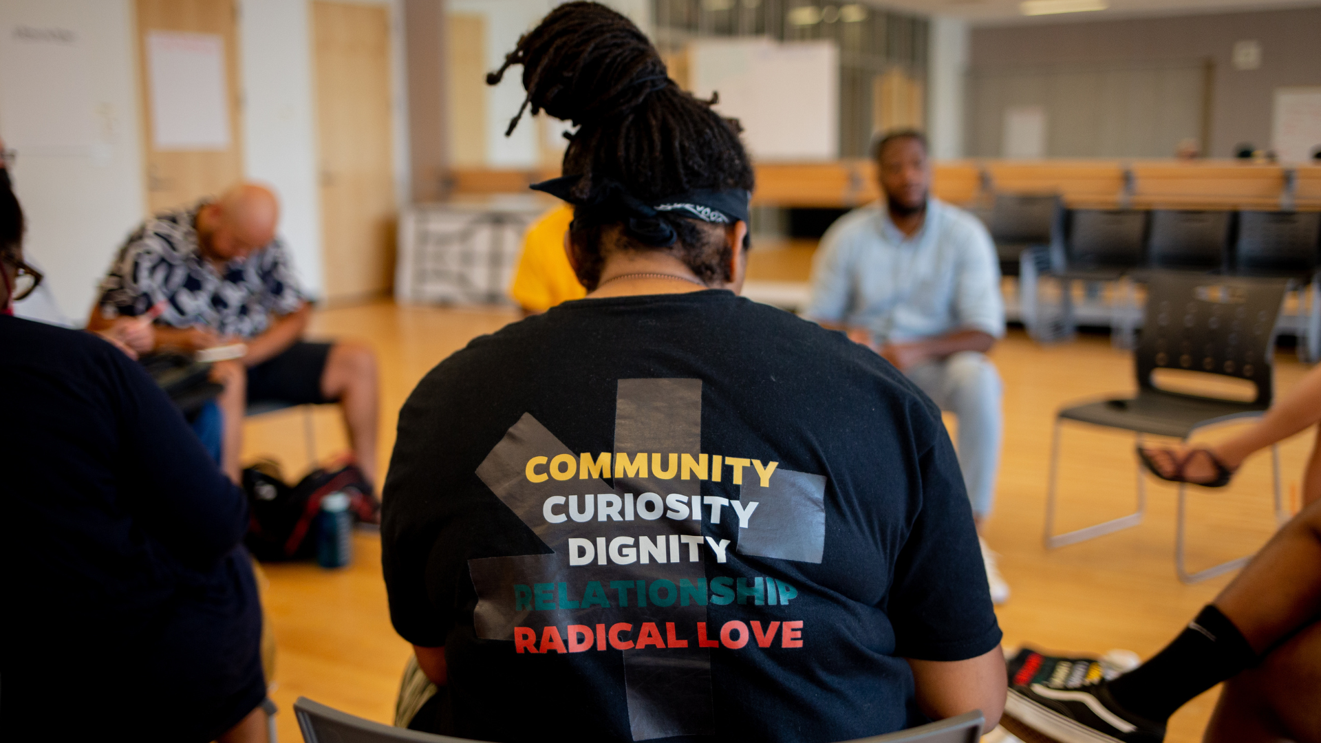 A woman wearing a black shirt with the words community, curiosity, dignity, relationships, and radical love on it.