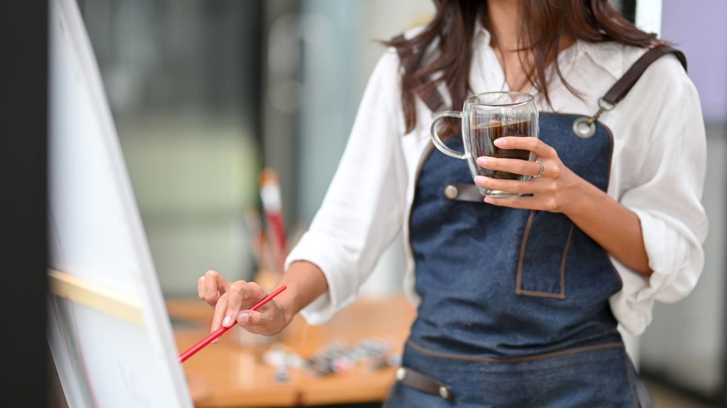 Woman holding cup of coffee with paintbrush and a canvas
