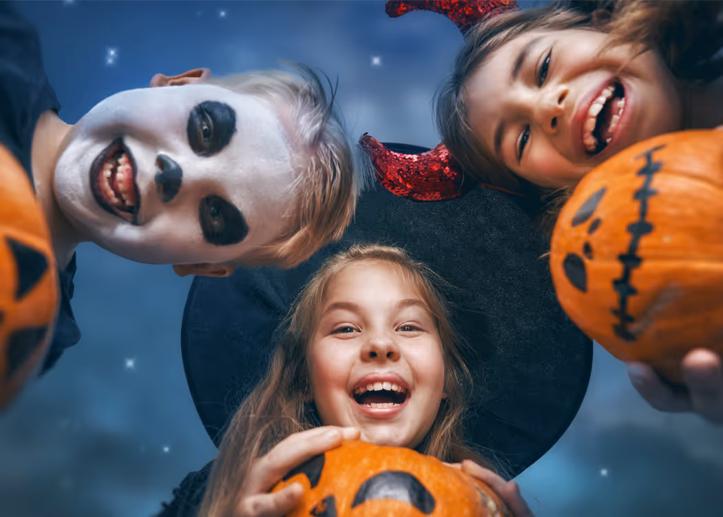 Three kids dressed in Halloween costume of witch, devil and ghost holding pumpkins