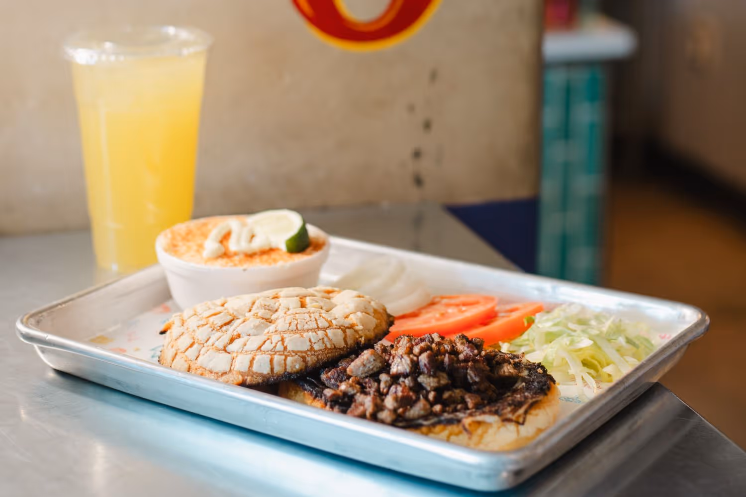 Concha sandwich on tray with a cup of elote and a drink