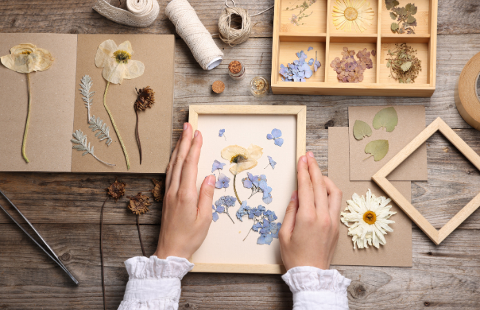 Image of hands holding hand made floral frame with dried yellow and purple flowers surrounded by dried flowers.