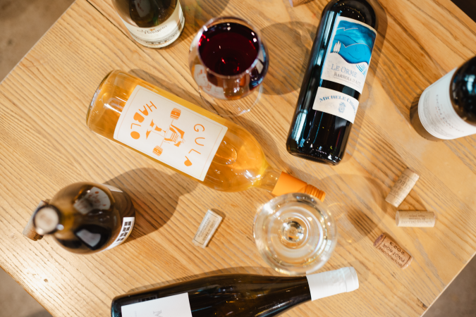 Table of various wines standing up and laying down, along with Wine glasses and corks.
