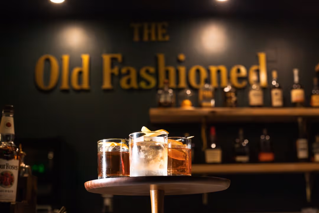 three old fashioned cocktails with topping, in front of signage for "The Old Fashioned" bar