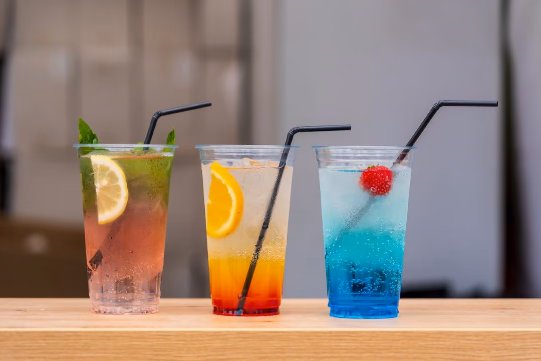 Three Fresca style drinks from left to right a pink beverage with a lemon and mint, a sunrise style drink with an orange, and a blue drink with a raspberry.