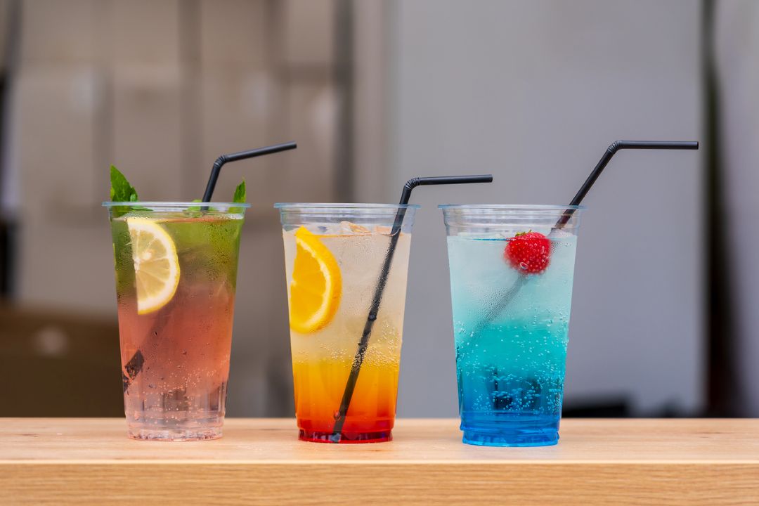 Three Fresca style drinks from left to right a pink beverage with a lemon and mint, a sunrise style drink with an orange, and a blue drink with a raspberry.