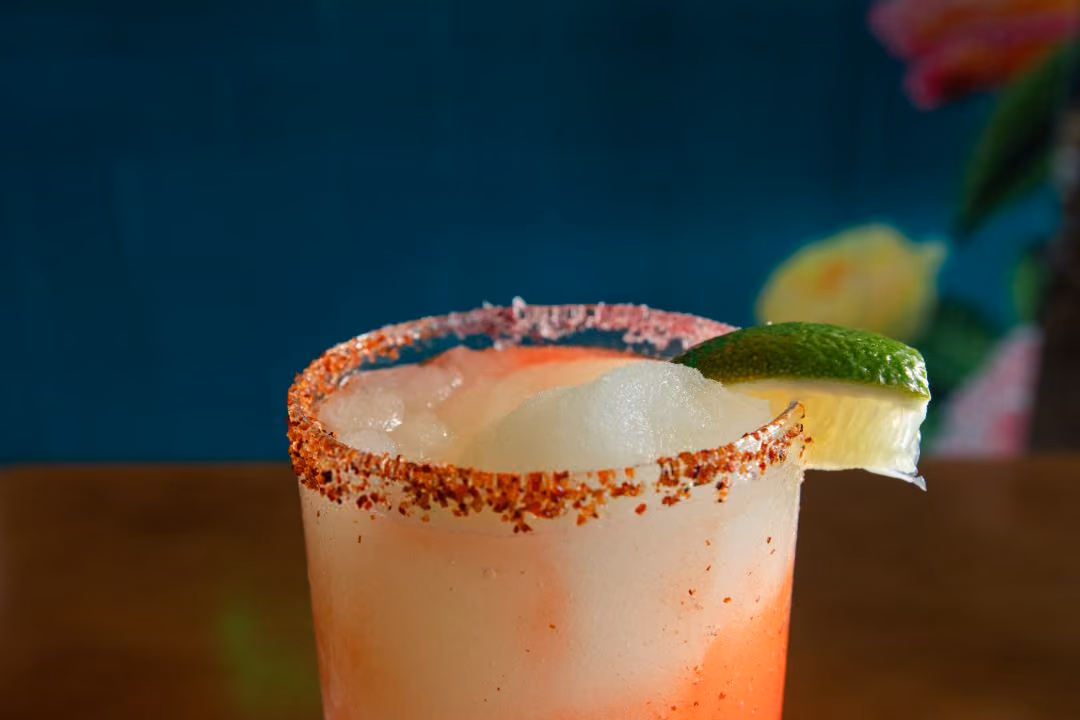Glass of Frozen Margarita with tajin rim and lime garnish on edge.