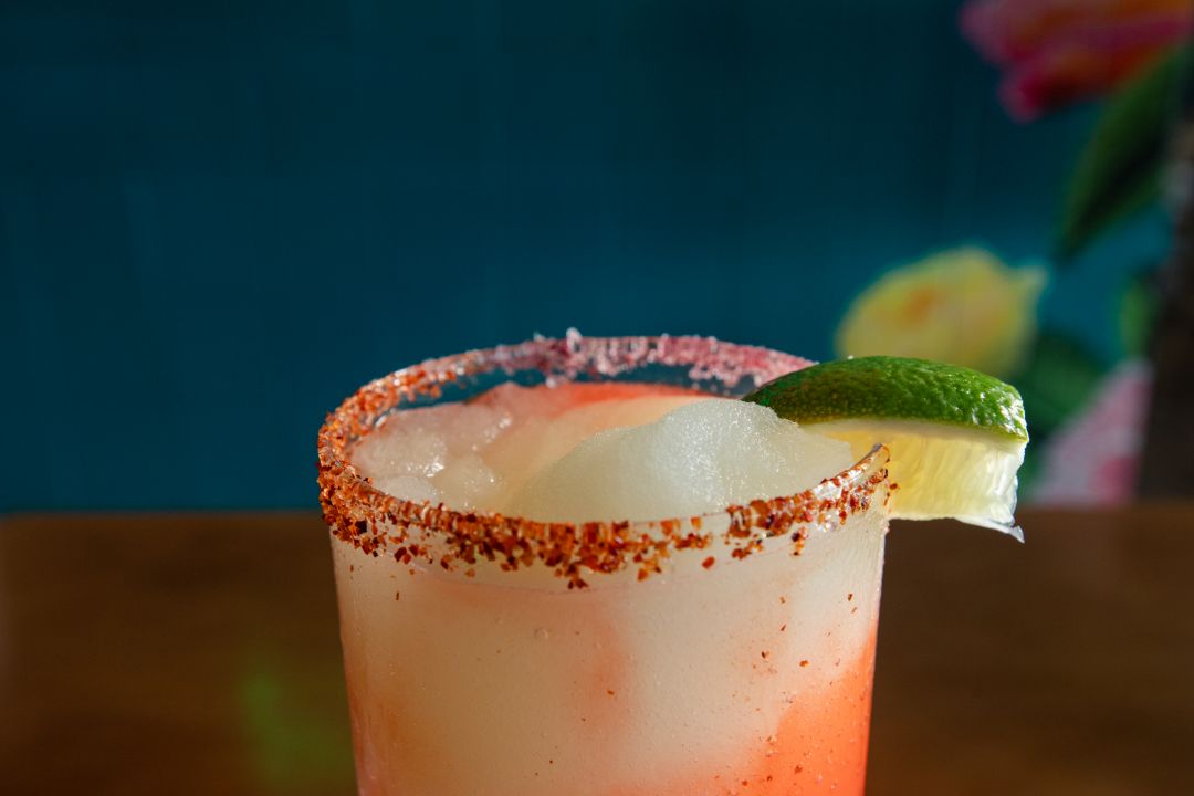 Glass of Frozen Margarita with tajin rim and lime garnish on edge.