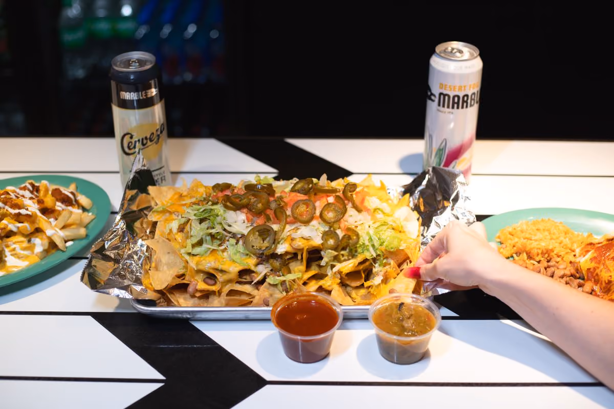 Hand reaching into a plate of Nachos with Beer in background