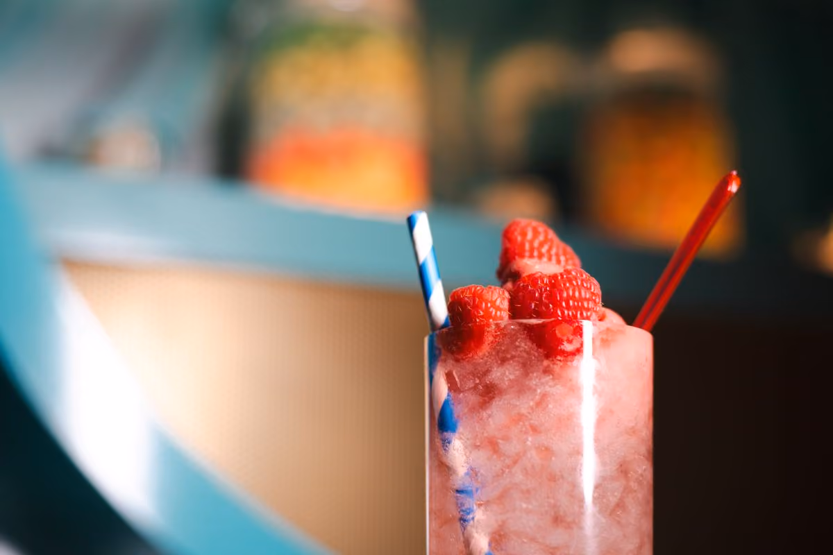 Pink Beverage with raspberries and cotton candy. Has blue striped straw and red spoon.