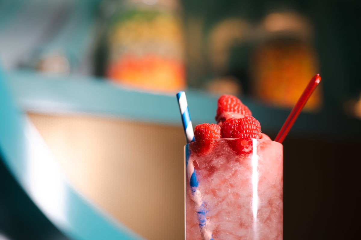 Pink Beverage with raspberries and cotton candy. Has blue striped straw and red spoon.