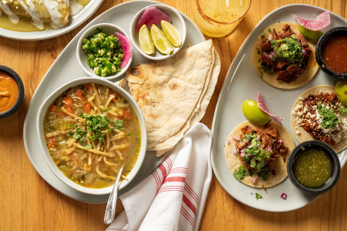 Overhead table view of Tortilla Stew with a side tortilla, also picture three tacos and sides of Salsa and crema