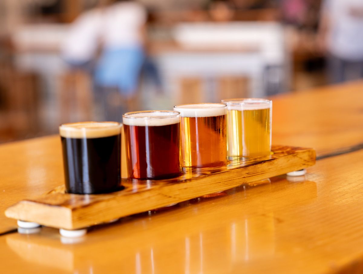 Four small glasses of beer on wood flight serving tray.