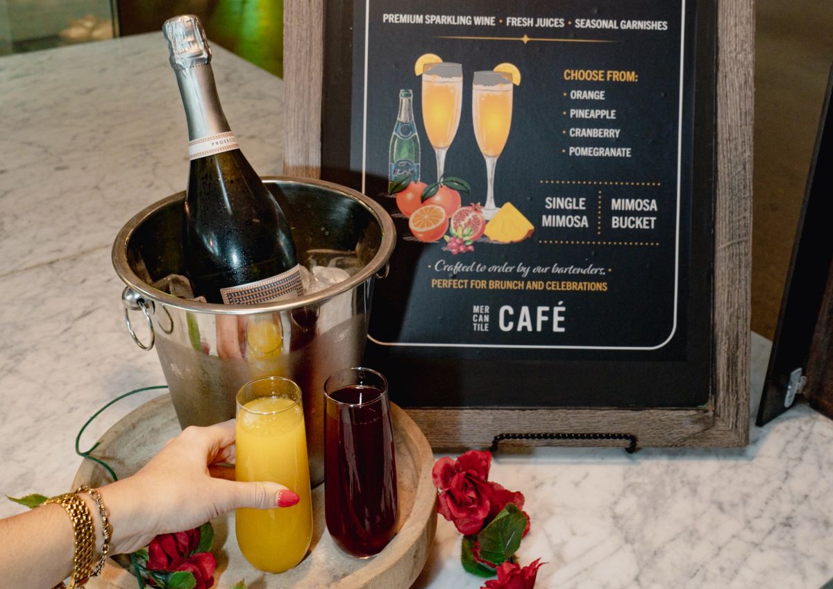 Sign displaying drink options for Mimosas bucket with sparkling wine, and two full glasses of different flavors. 