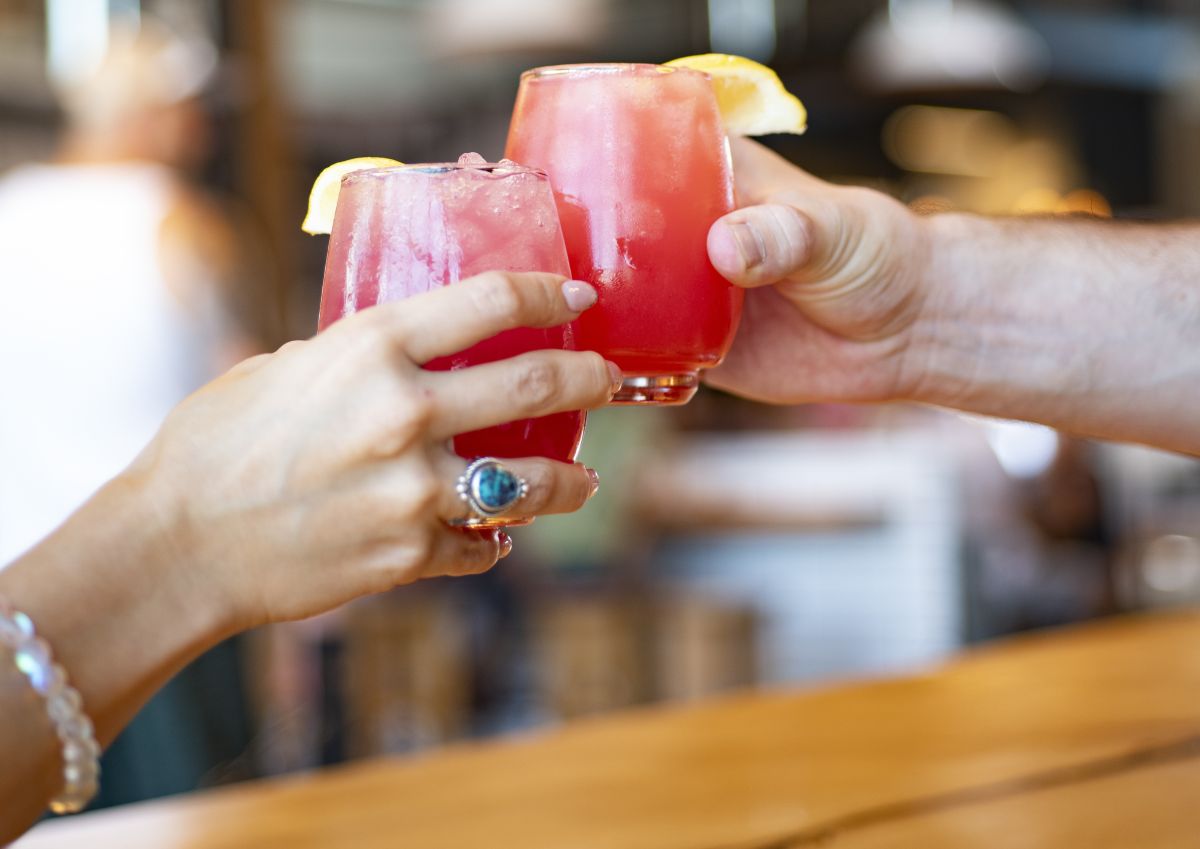 Two hands toasting red cocktail beverage with lemon wedges. 