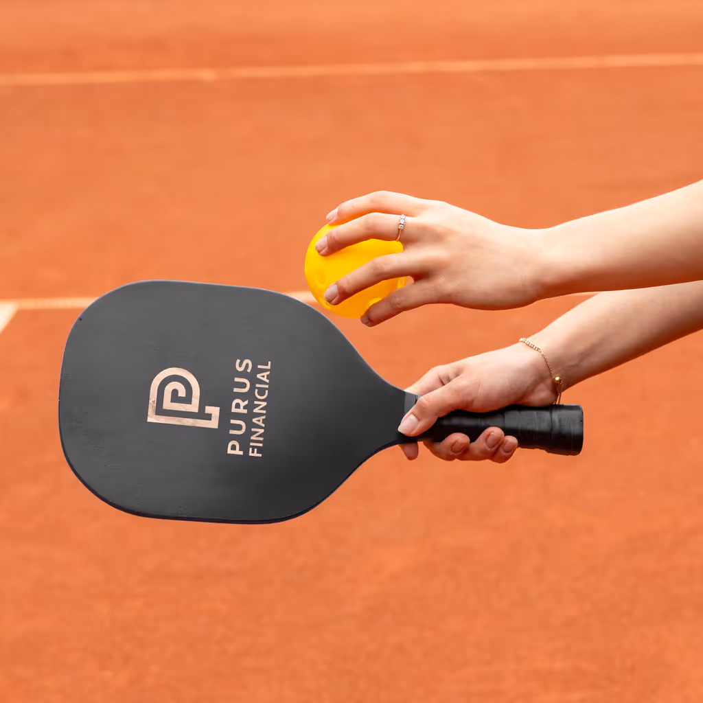 A black branded pickleball paddle prepared to serve a pickleball