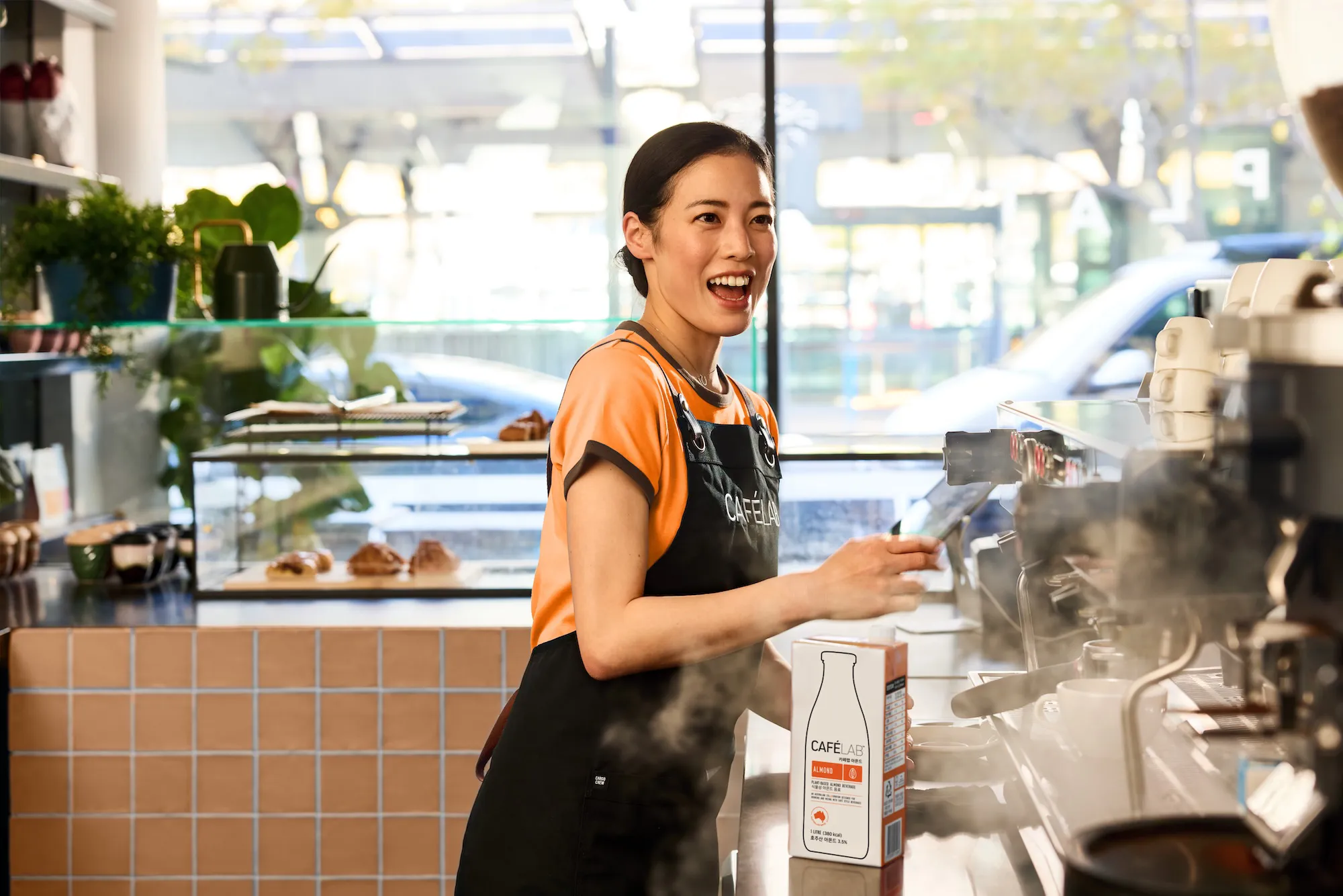 카페에서 에스프레소 머신을 사용하며 미소 짓는 검은 머리 여직원.