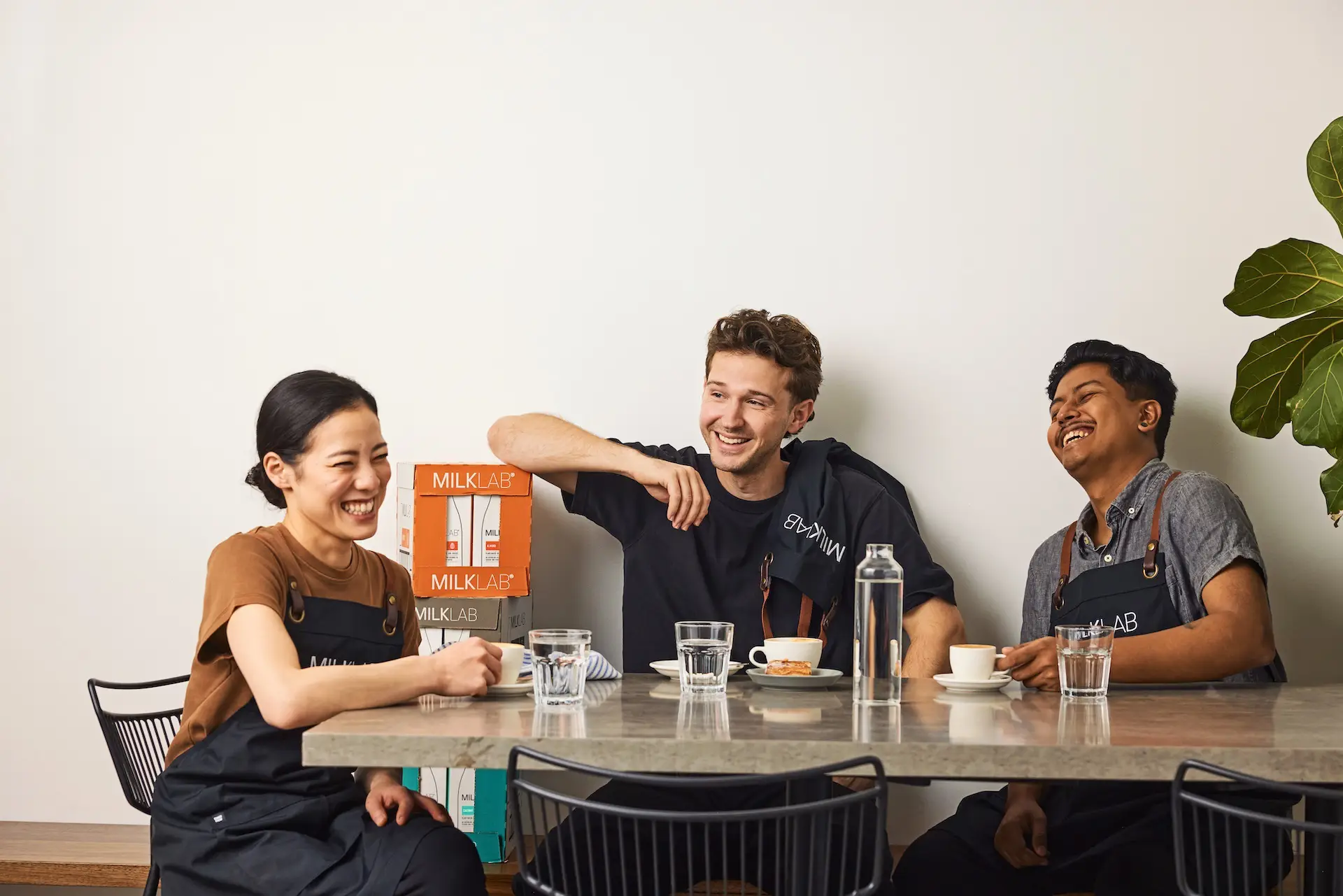 Three baristas sitting at a table, smiling and enjoying coffee together with glasses of water.