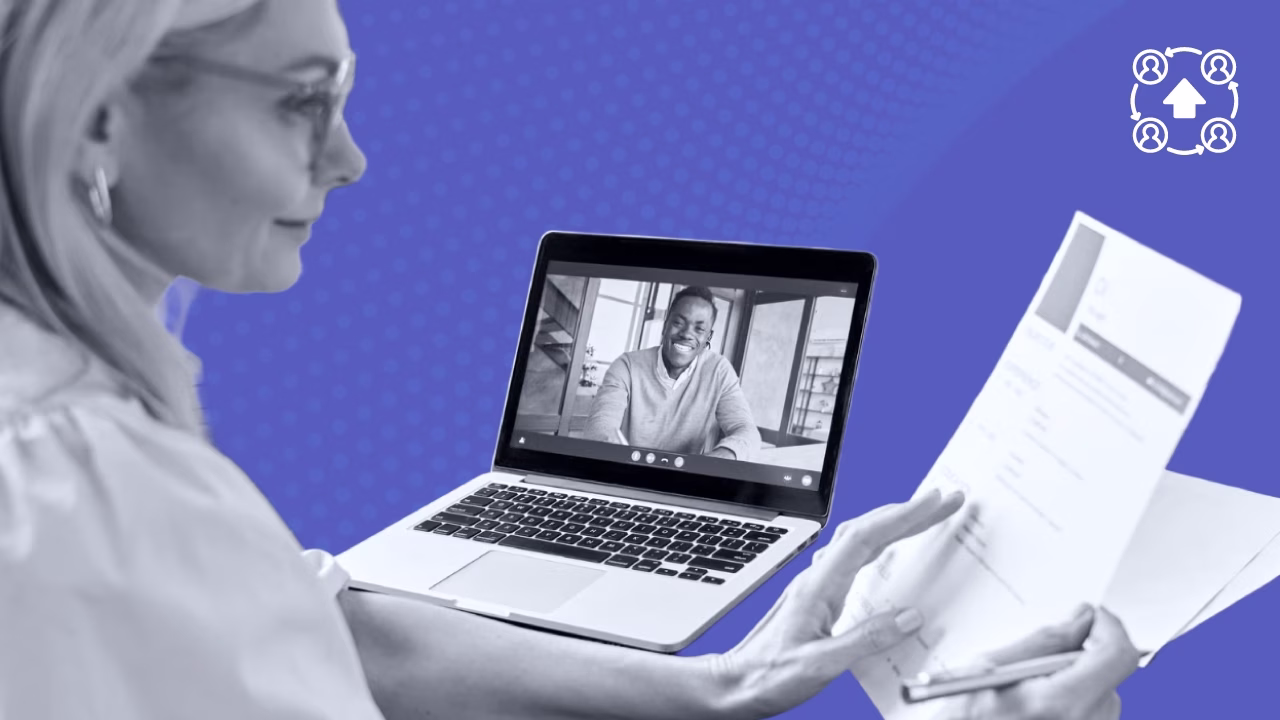 Woman in glasses reviewing documents while video chatting with man on a laptop in a purple background.
