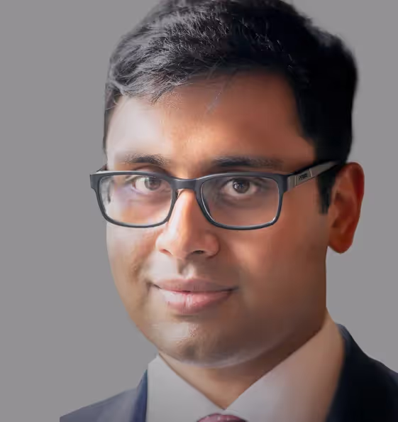 Headshot of Sashank Srinivasan;Photo of a young man with black framed glasses and black hair. He is wearing a black blazer and white shirt. The background of the picture is grey.