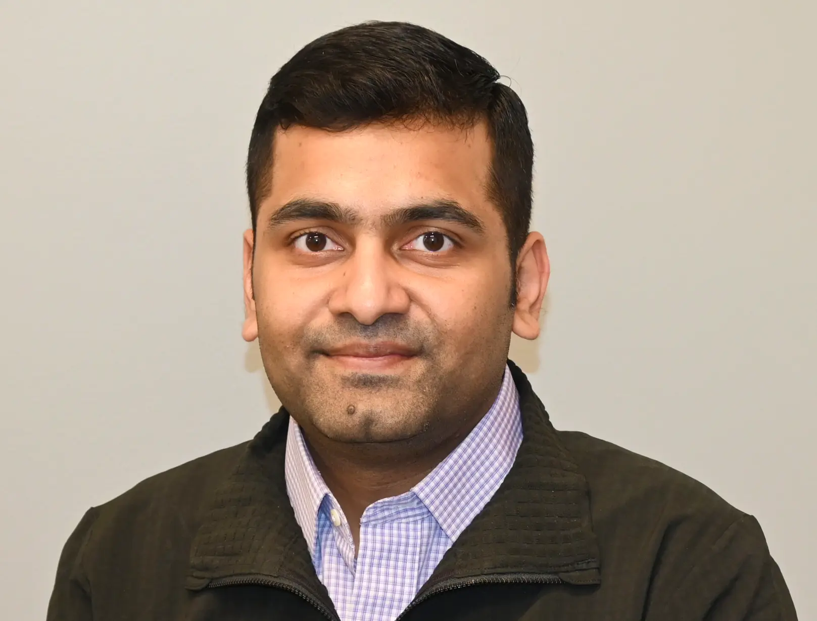 Photo of Mohit Jaju; Professional headshot of a smiling man with short dark hair, wearing a checkered shirt and dark jacket against a neutral background.