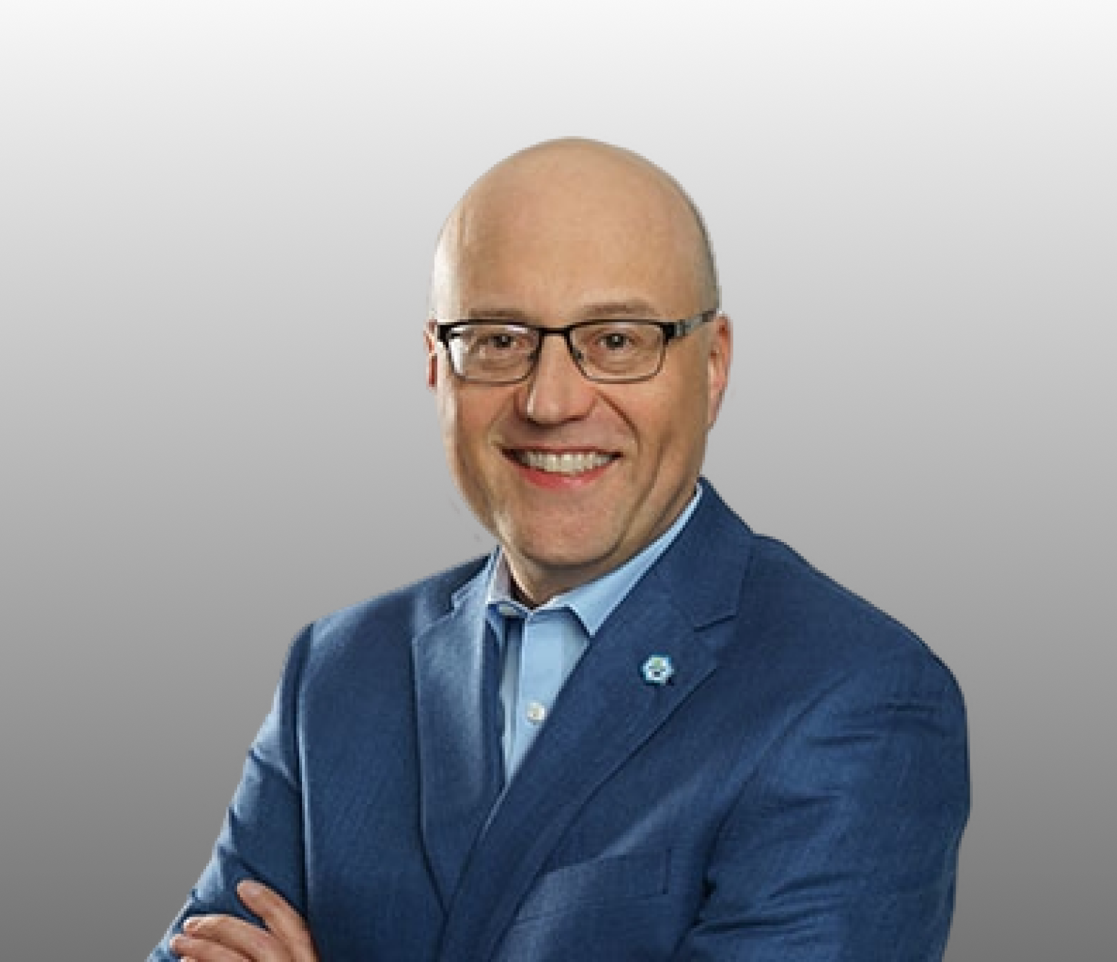 Photo of Rob Bodor; Close-up portrait of a smiling bald man with glasses, wearing a blue suit jacket over a light blue collared shirt with a small lapel pin against a plain gray background.