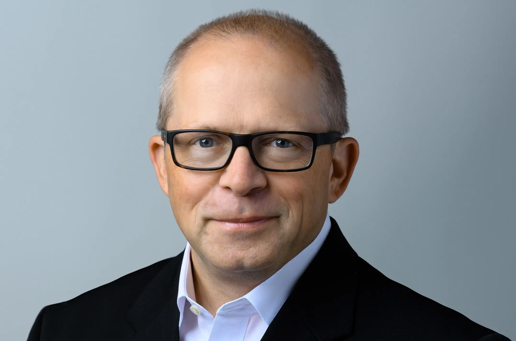 Graphic from the article Msa Safety Pioneering Protective Solutions; A professional photograph of a man with black framed glasses and thin hair, wearing a black blazer and white shirt. He has a small smile on his face.