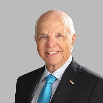 Photo of Bill Priest; Photo of a very elderly man wearing a black blazer, white check shirt and blue tie. He has a big smile on his face and a pin on his lapel.