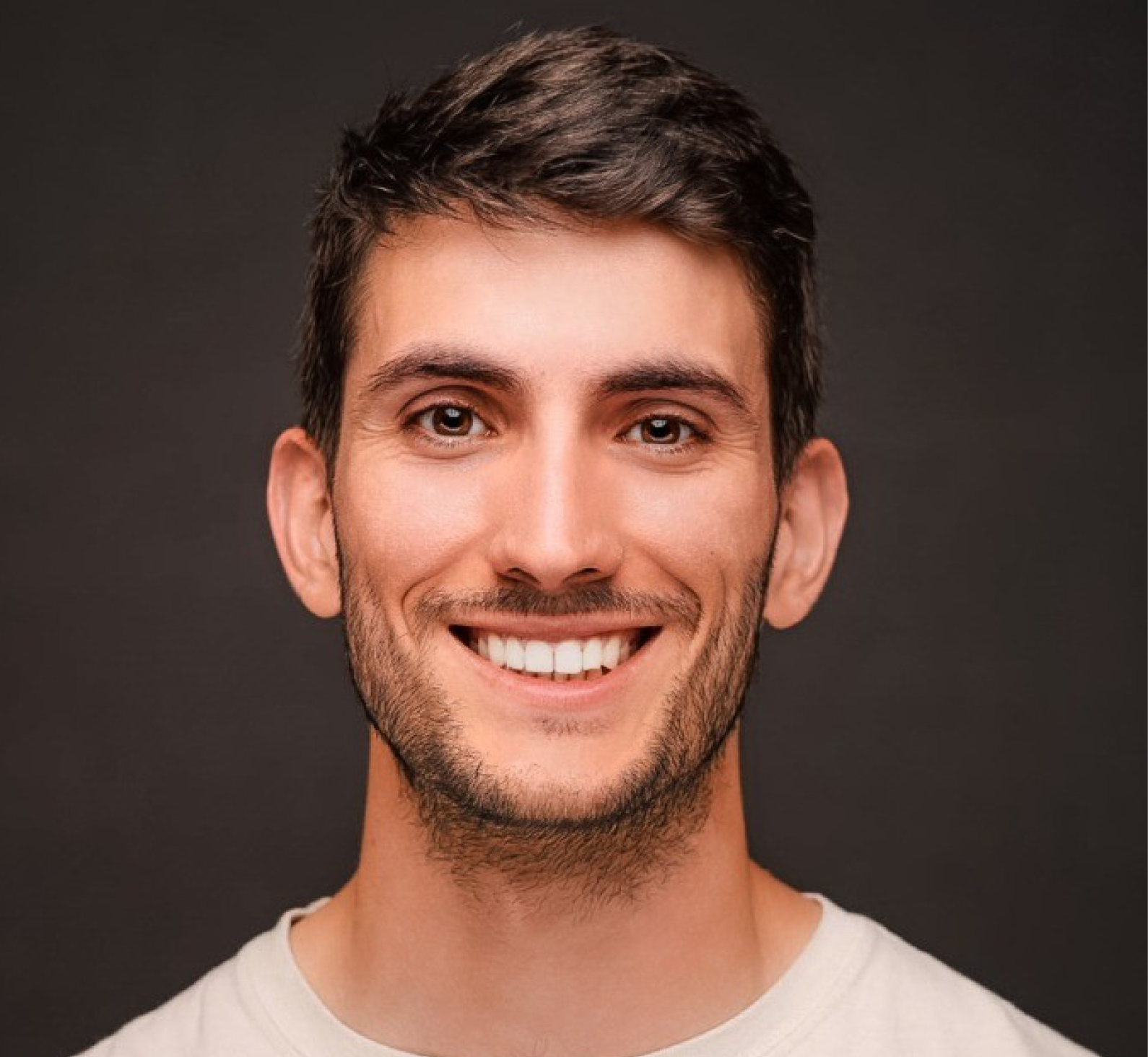 Photo of Paulo; Portrait of a smiling young man with dark hair and light stubble, wearing a white shirt against a dark background; warm, friendly expression.