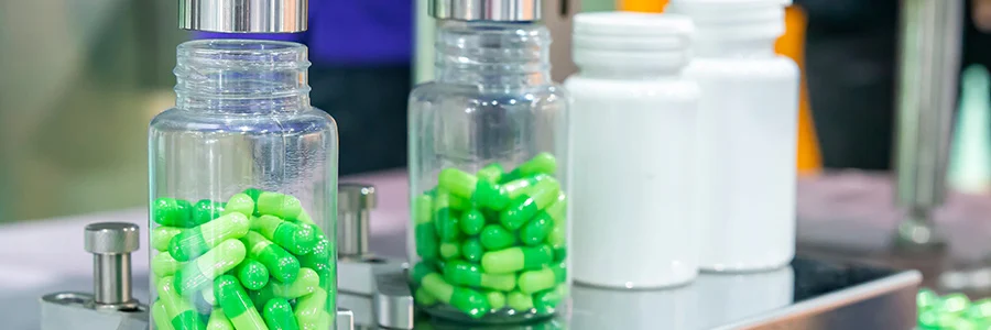 A photo of an automated pharmaceutical production line with machines filling bottles with medicine capsules