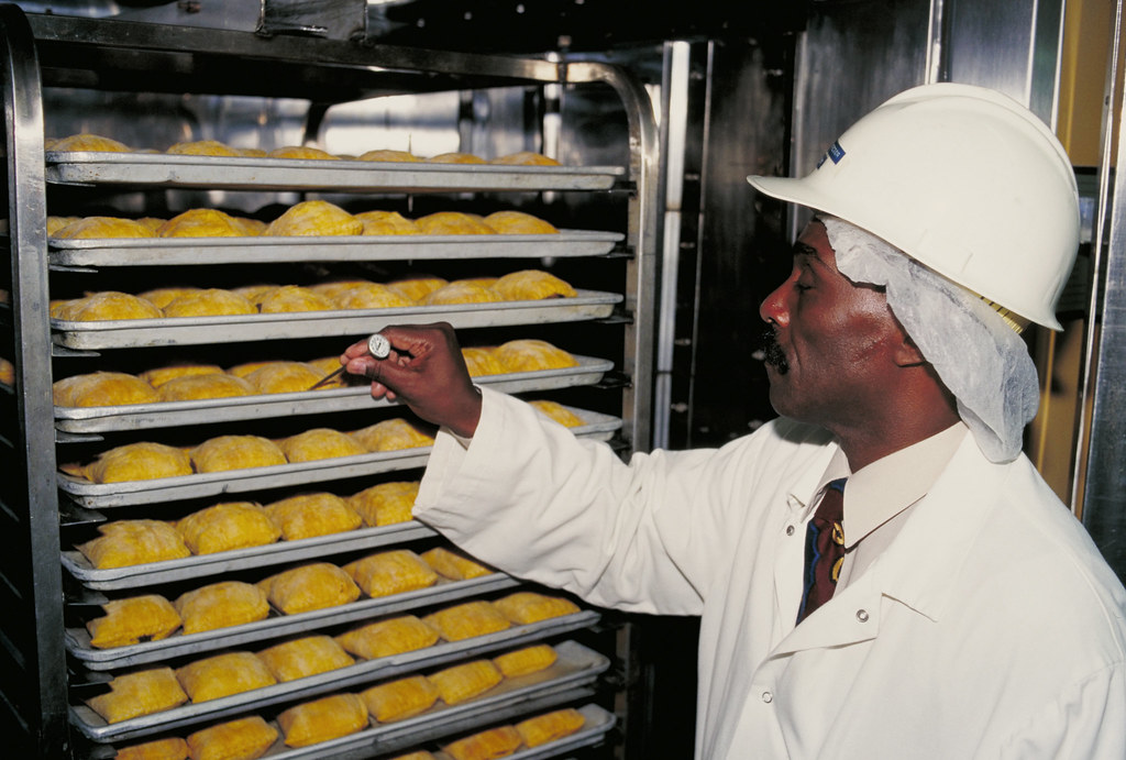 Inspector con bata y casco controlando bandejas de producción