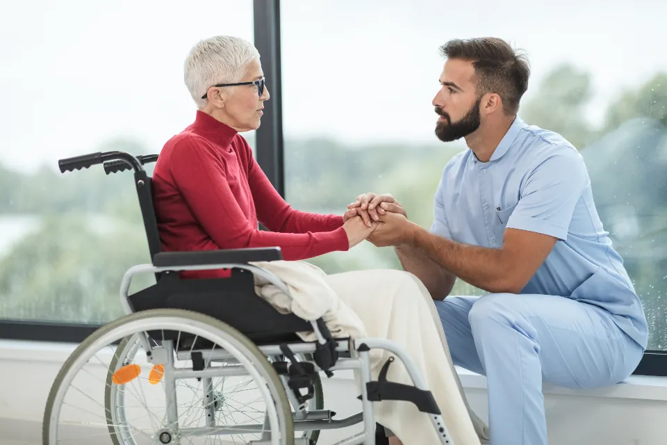 Aide-soignant tenant la main d'une personne âgée en fauteuil