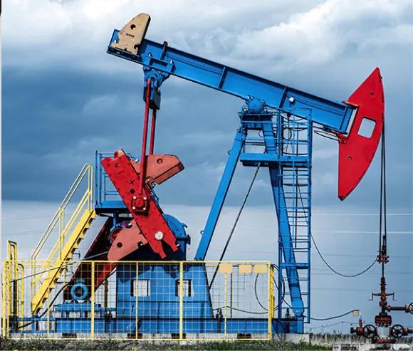 Blue and red oil pumpjack under a cloudy sky with yellow safety railing around it.