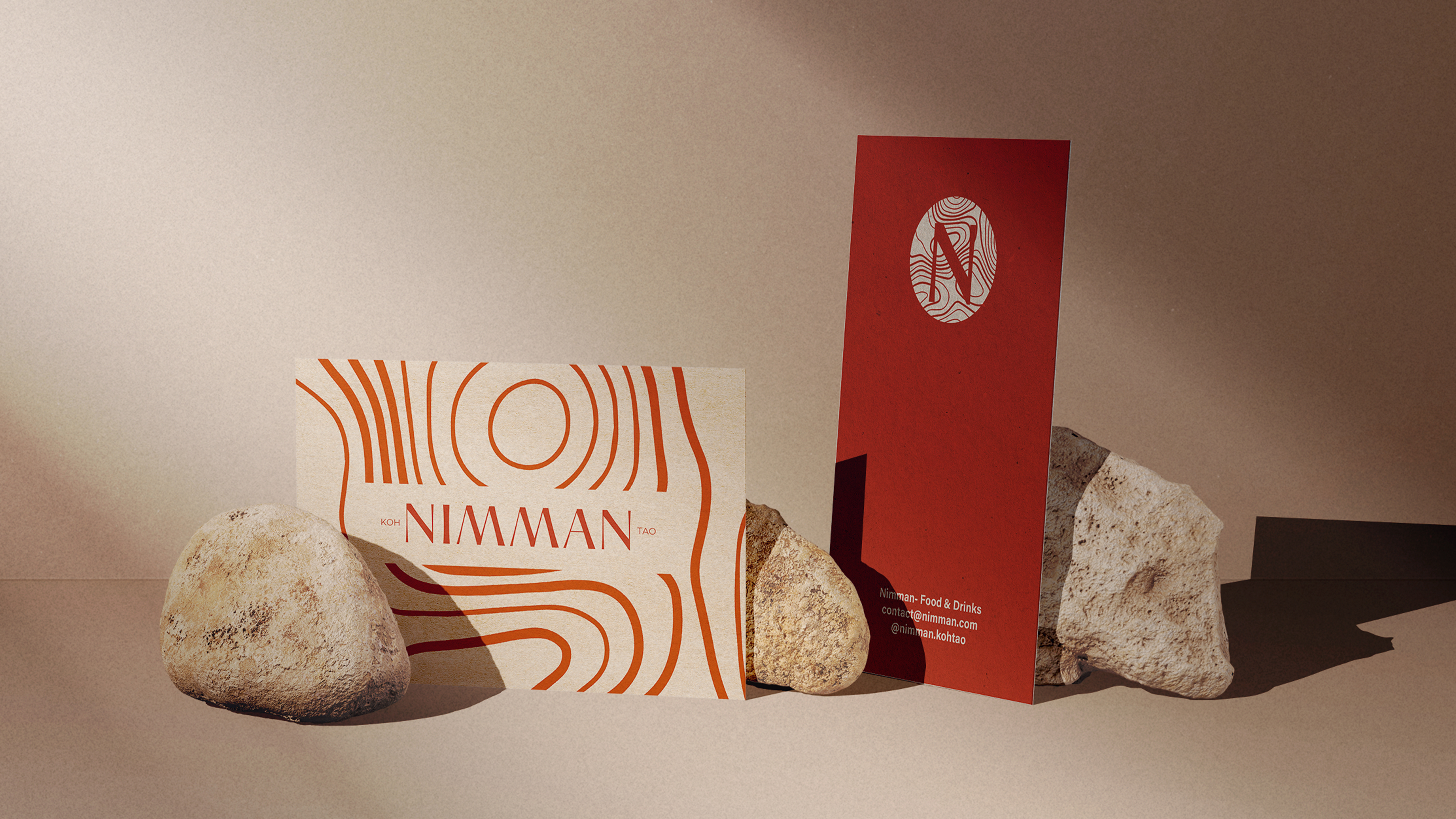 Cartes de visite stylisées avec motifs organiques orange, appuyées contre des pierres sur un fond beige.