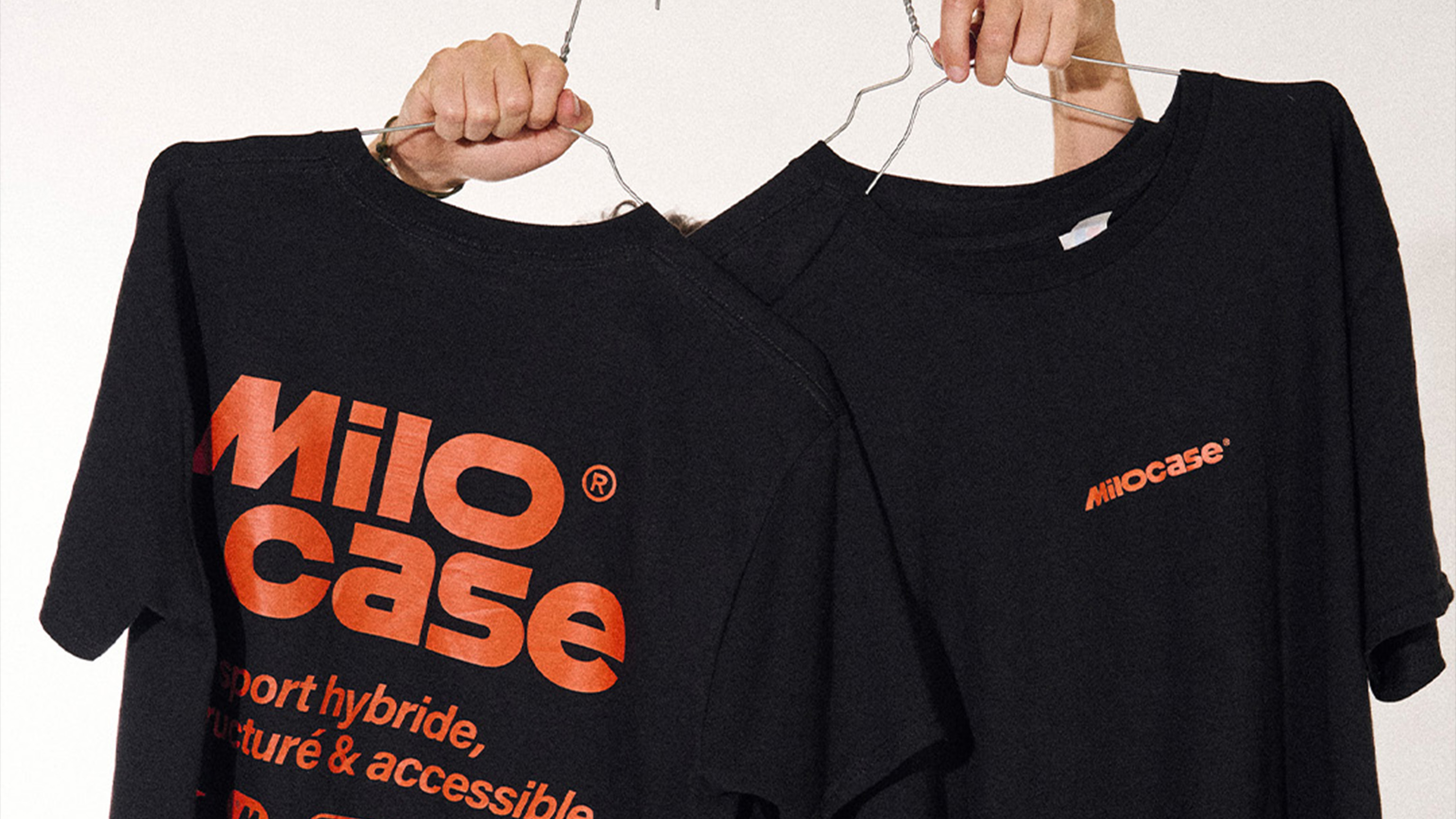 Deux t-shirts noirs suspendus, l'un avec le grand logo orange "Milocase" et du texte en dessous, l'autre avec un petit logo "Milocase".
