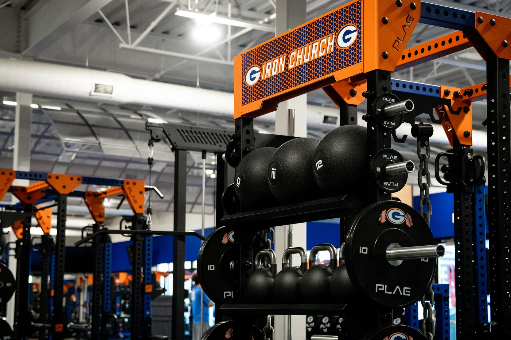 Custom branded PLAE ICONx rack with integrated storage for medicine balls, kettlebells and weight plates in a collegiate performance facility.