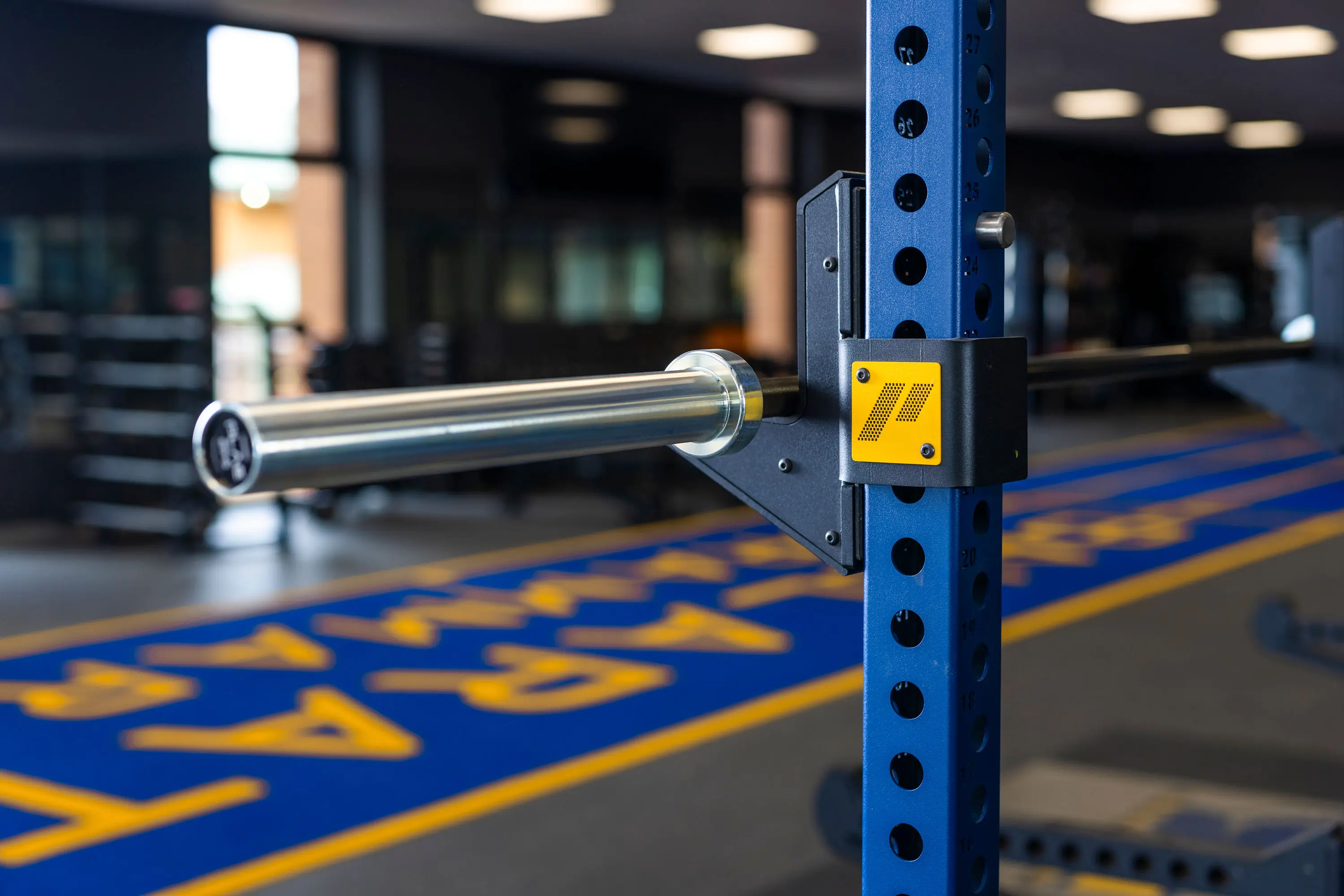 Close-up of a PLAE ICON X rack upright and barbell J-cup overlooking the blue Ballarat Grammar ATTACK turf sprint track