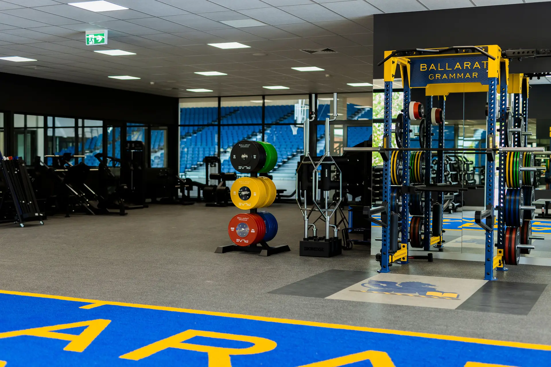 PLAE ICON X rack and colour-coded PLAE bumper plate tree on the Ballarat Grammar gym floor, with windows overlooking the school stadium