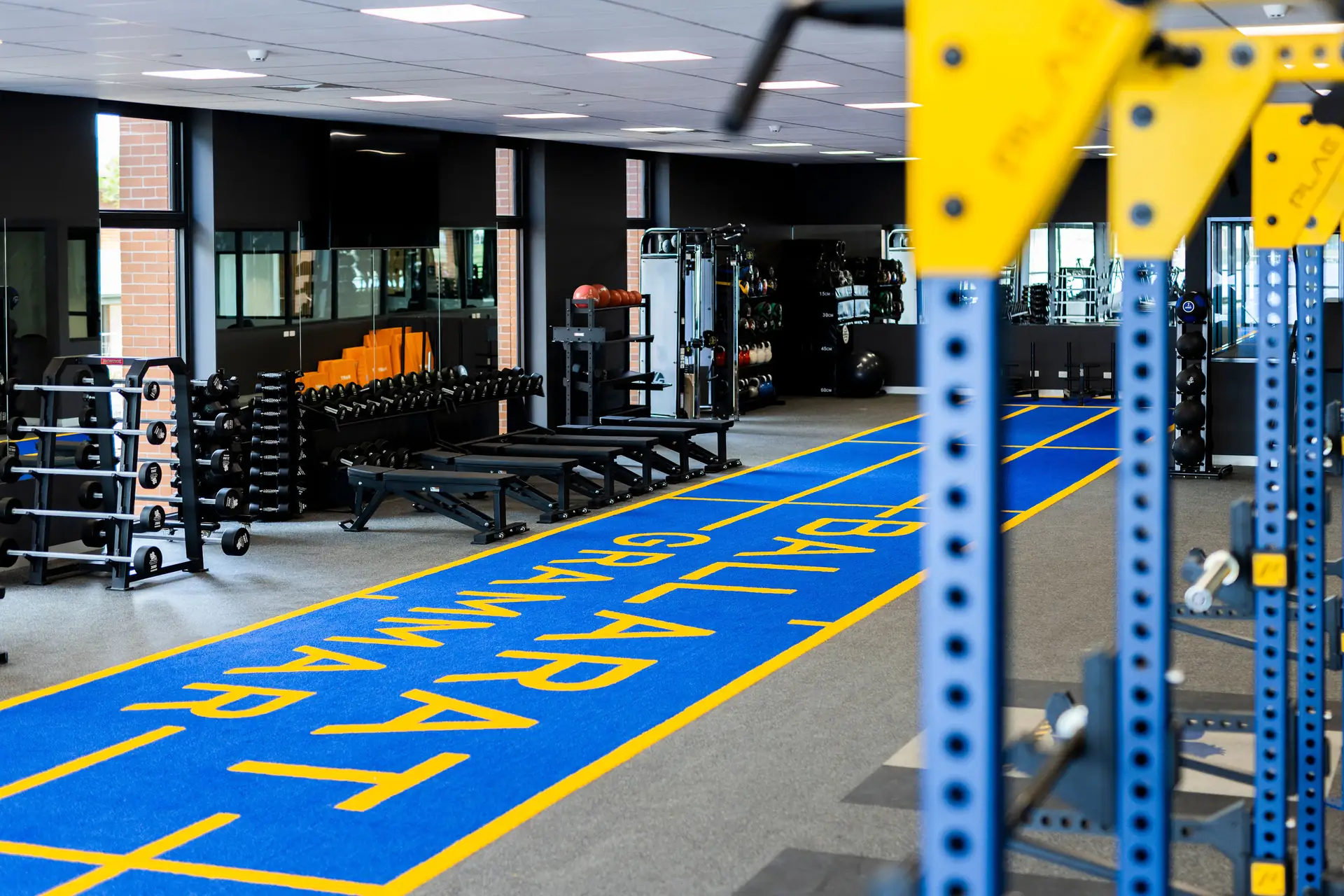 Ballarat Grammar strength and conditioning gym with the blue ATTACK turf track, PLAE dumbbell racks, benches and colour-coded bumper plate trees